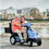 Couple Driving Dual Seat Recreational Scooter On Boardwalk. Couple Driving Dual Seat Recreational Scooter On Boardwalk.