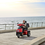Afiscooter S 3-Wheel By Afikim In Red Driving On Pier. Afiscooter S 3-Wheel By Afikim In Red Driving On Pier.